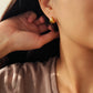 Close-up of a person wearing gold earrings with a neutral background