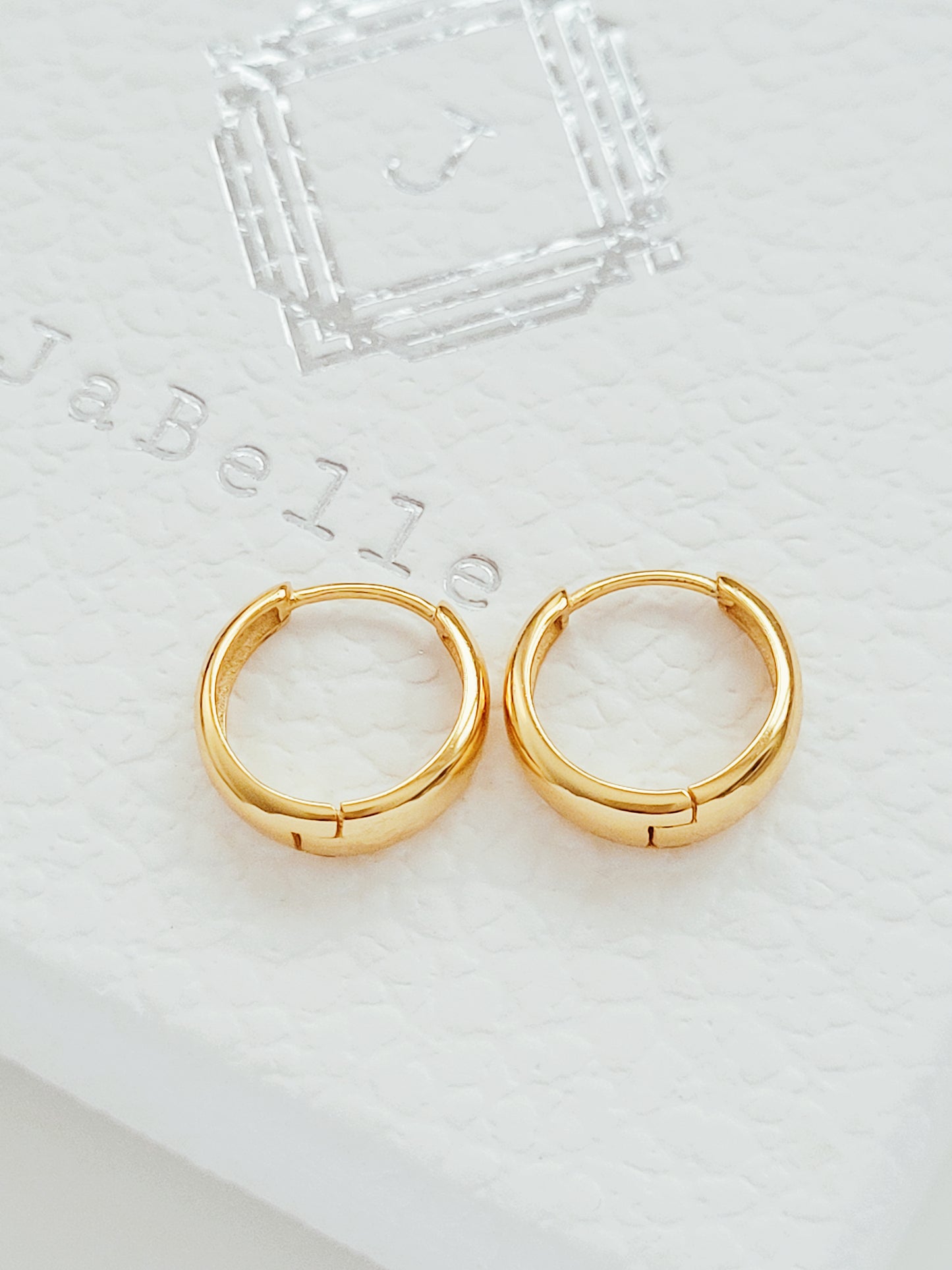 A pair of exquisite tapered gold hoop earrings displayed on a sleek white box, embodying timeless elegance and style.