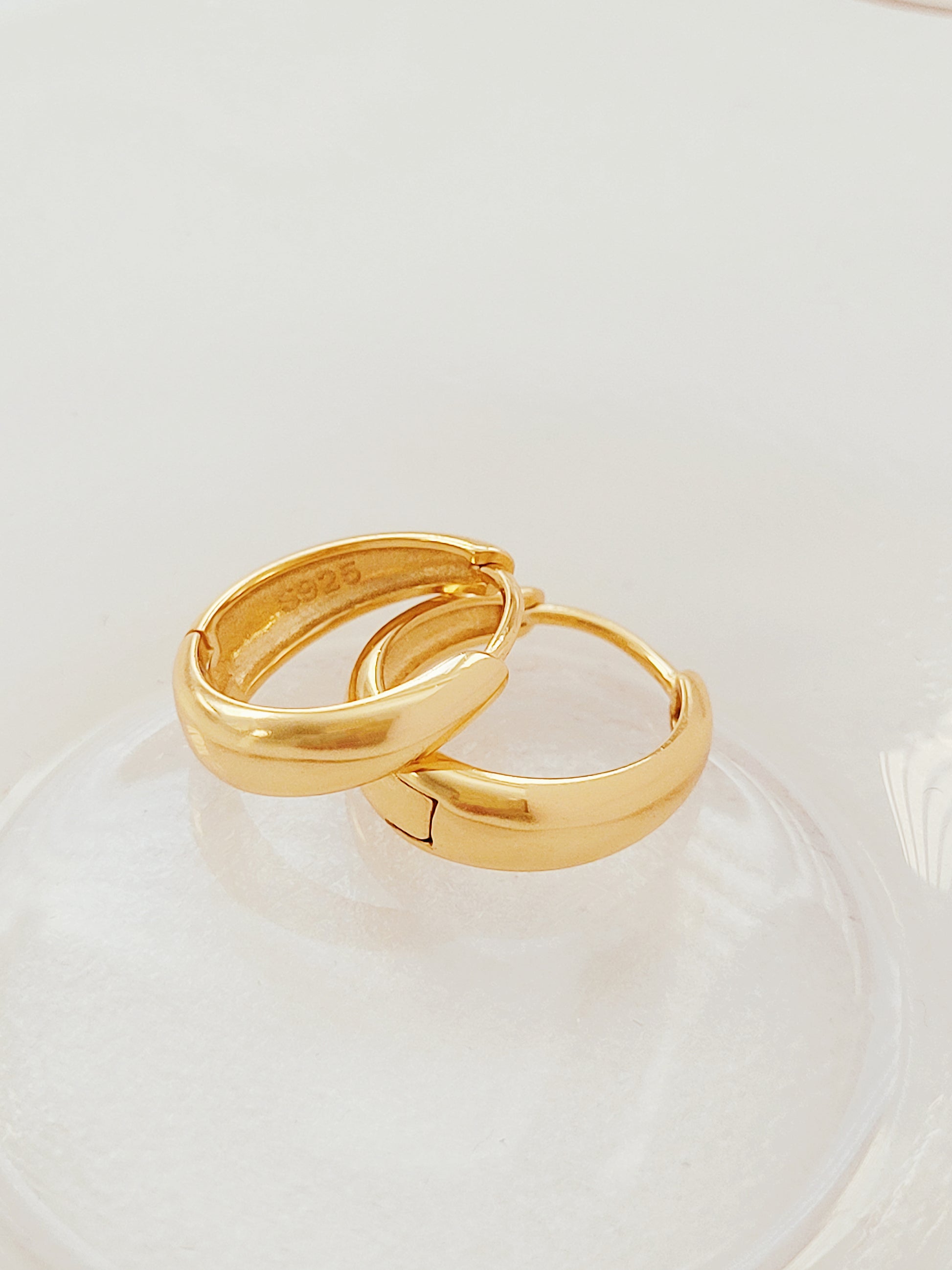 Two elegant tapered gold hoop earrings resting gracefully on glass table, exuding luxury and sophistication.