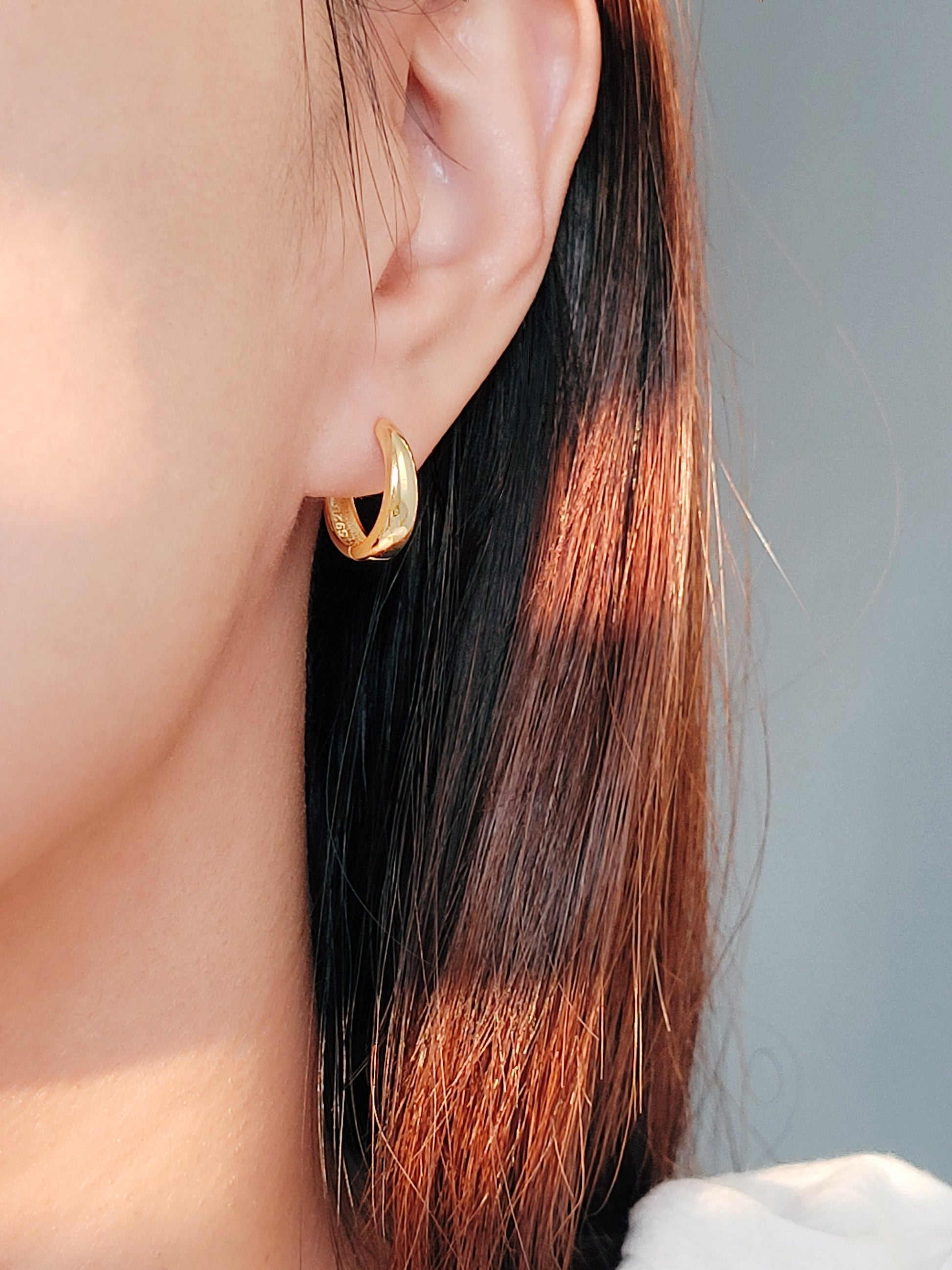 A stylish woman adorned with tapered gold hoop earrings, exuding grace and luxury in her refined look.