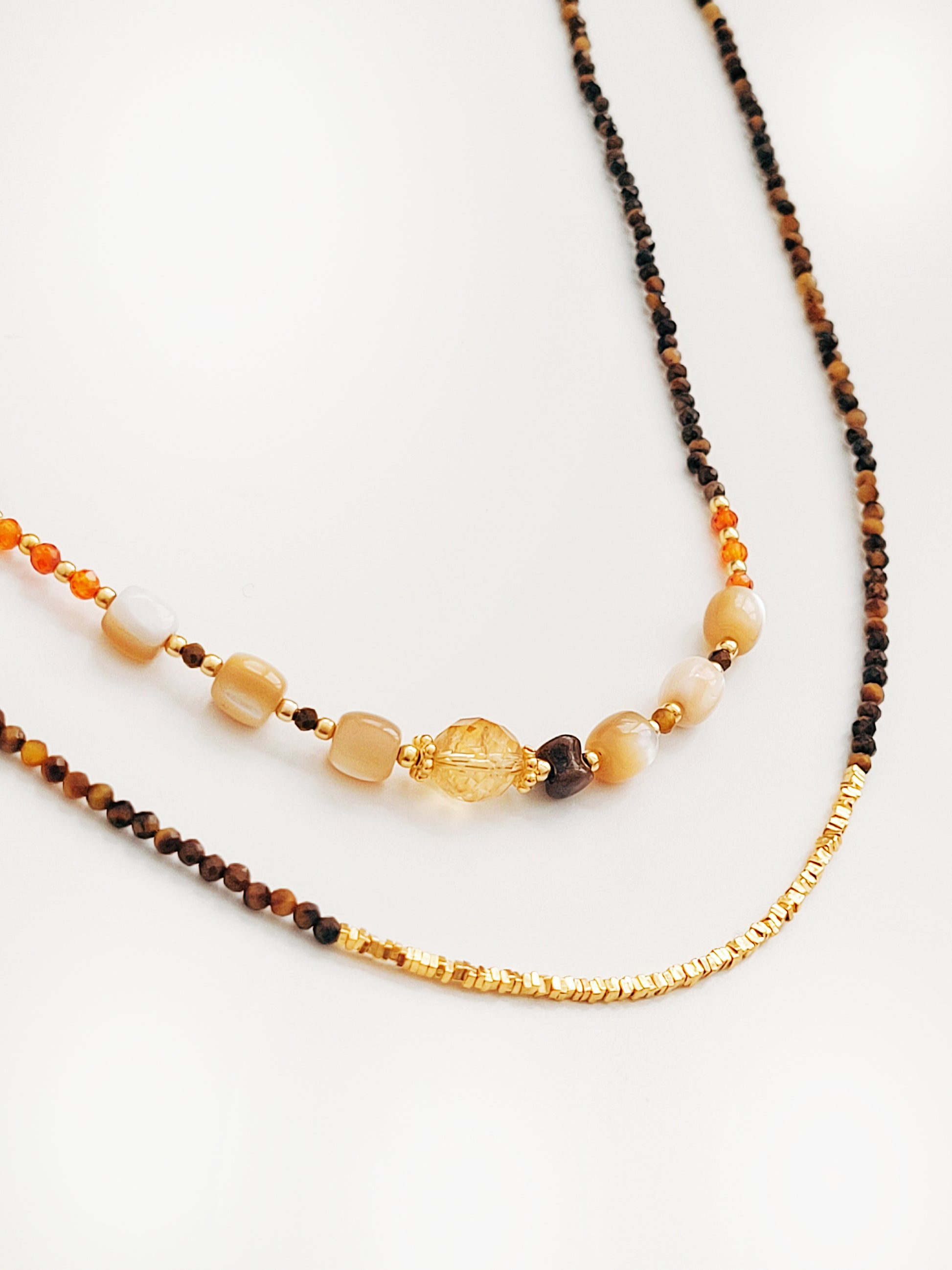 Close-up of a gemstone necklace featuring Tiger’s Eye gemstone with 22K gold vermeil nugget beads on white surface