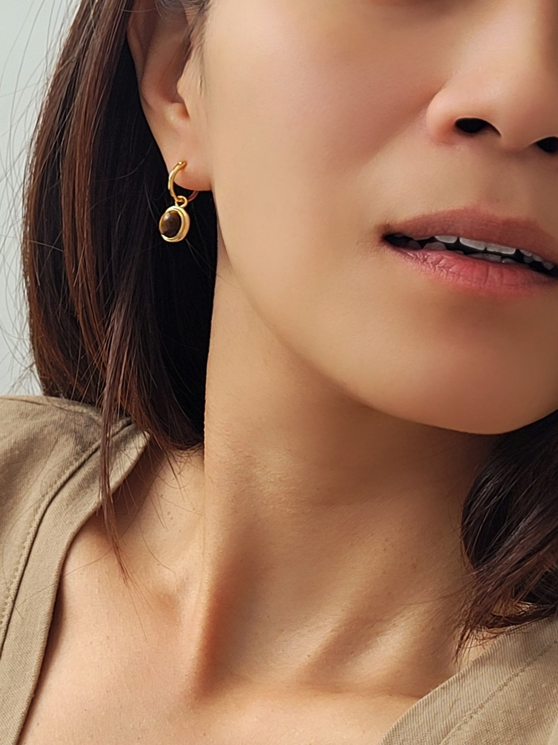 A model wearing a tiger's eye gemstone dangle earring in  minimalist and elegant style.