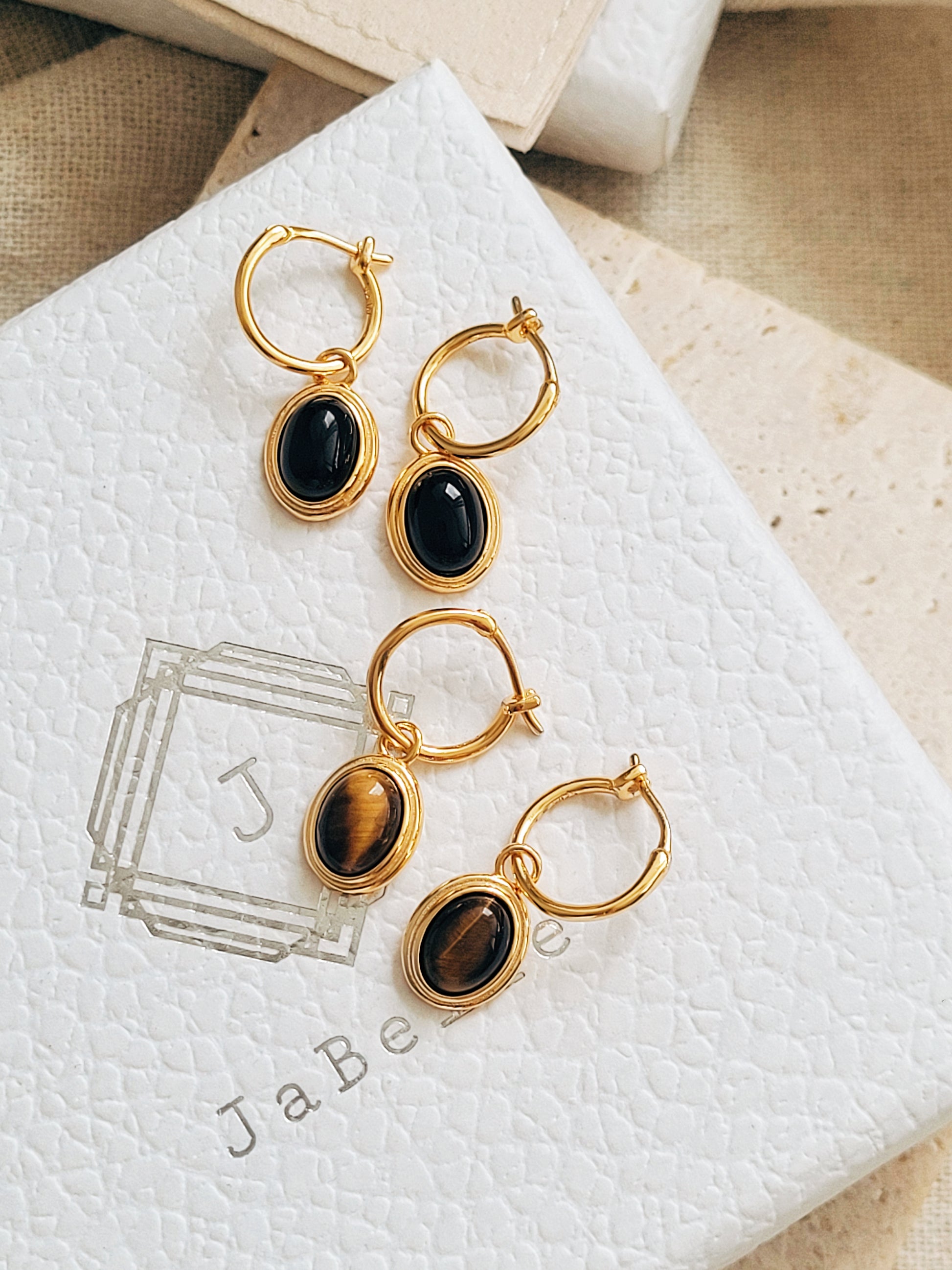 Close-up of gold vermeil dangle earrings with an oval black onyx gemstone or tiger's eye gemstone on a jewellery box, minimalist and elegant style