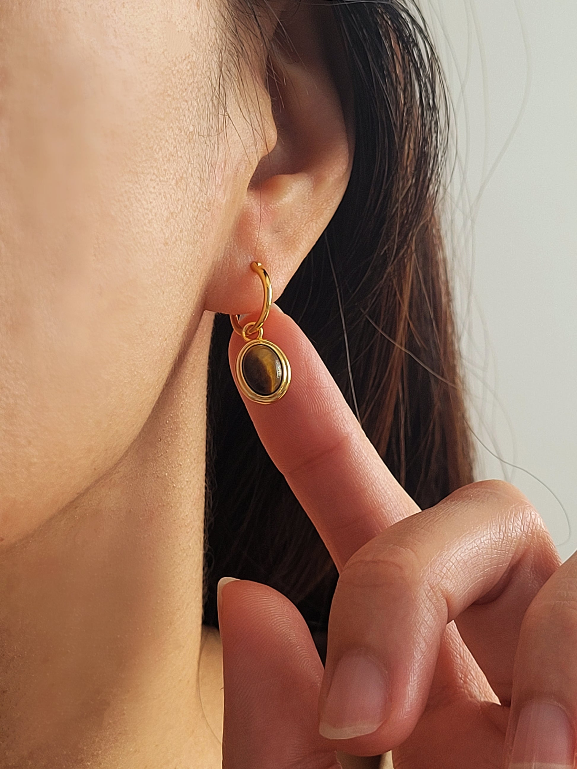 A tiger's eye oval gemstone earring worn on a woman's ear showcasing its details and exquisite craftmanship