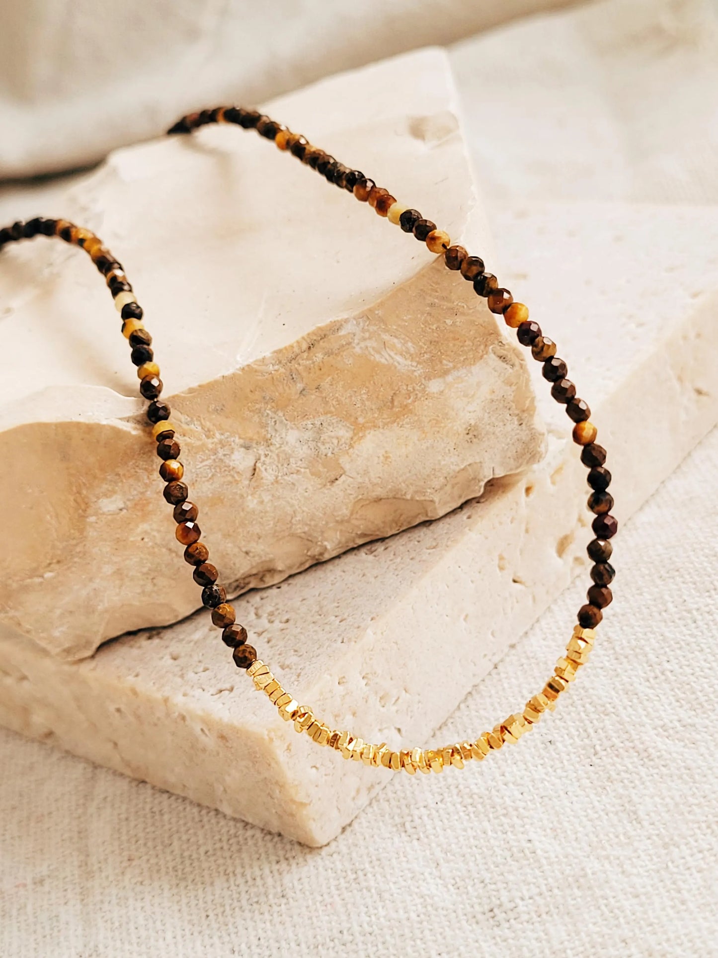 A delicate necklace with brown tiger's eye gemstone and gold vermeil beads on a stone surface.
