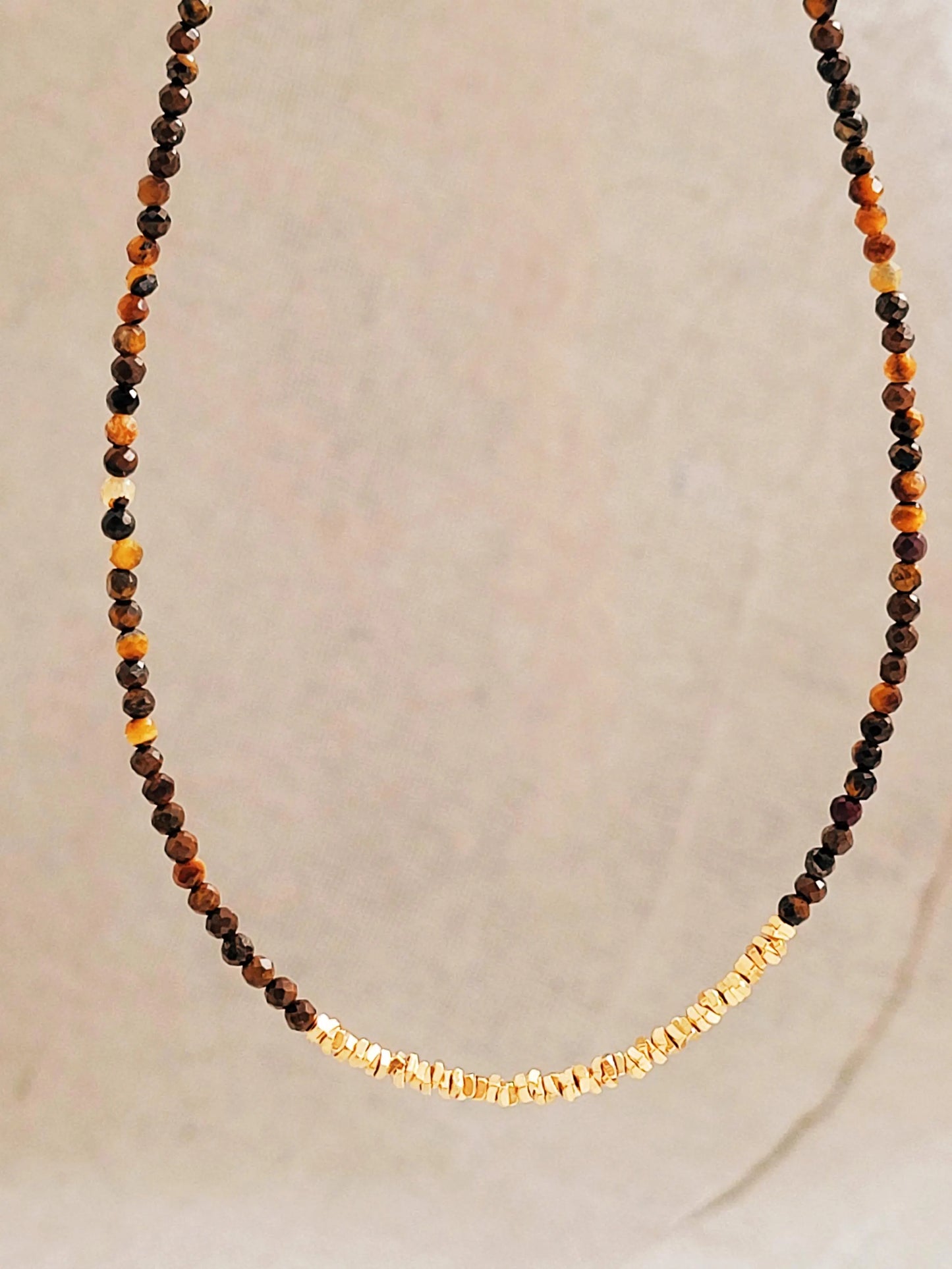Necklace with natural tiger's eye gemstone and gold accents on a neutral background