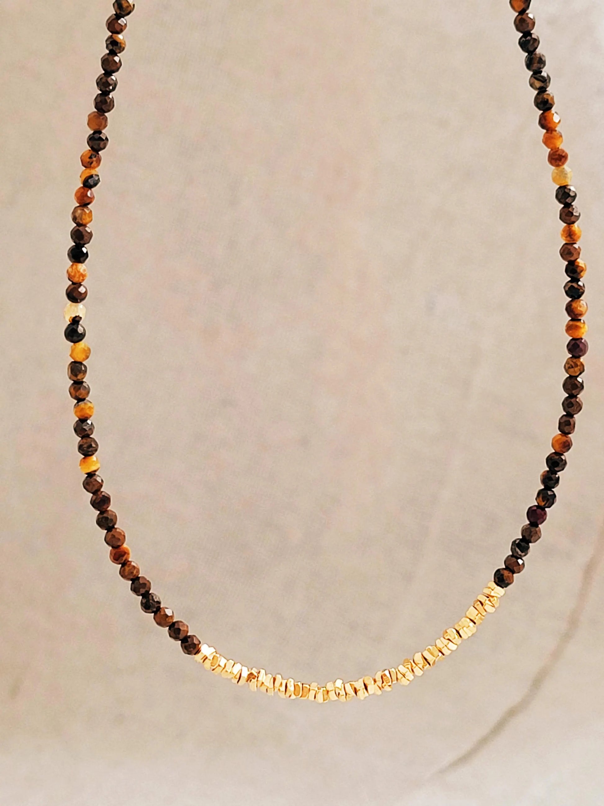 Necklace with natural tiger's eye gemstone and gold accents on a neutral background