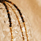 Minimal gold tiger's eye beaded choker necklace with gold vermeil accents displayed on textured glass, styled in warm beige aesthetic for a soft, luxury jewellery look.