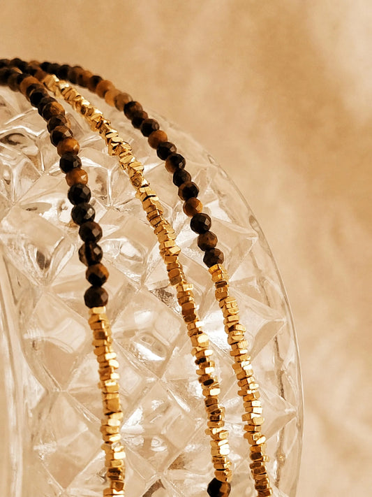 Minimal gold tiger's eye beaded choker necklace with gold vermeil accents displayed on textured glass, styled in warm beige aesthetic for a soft, luxury jewellery look.
