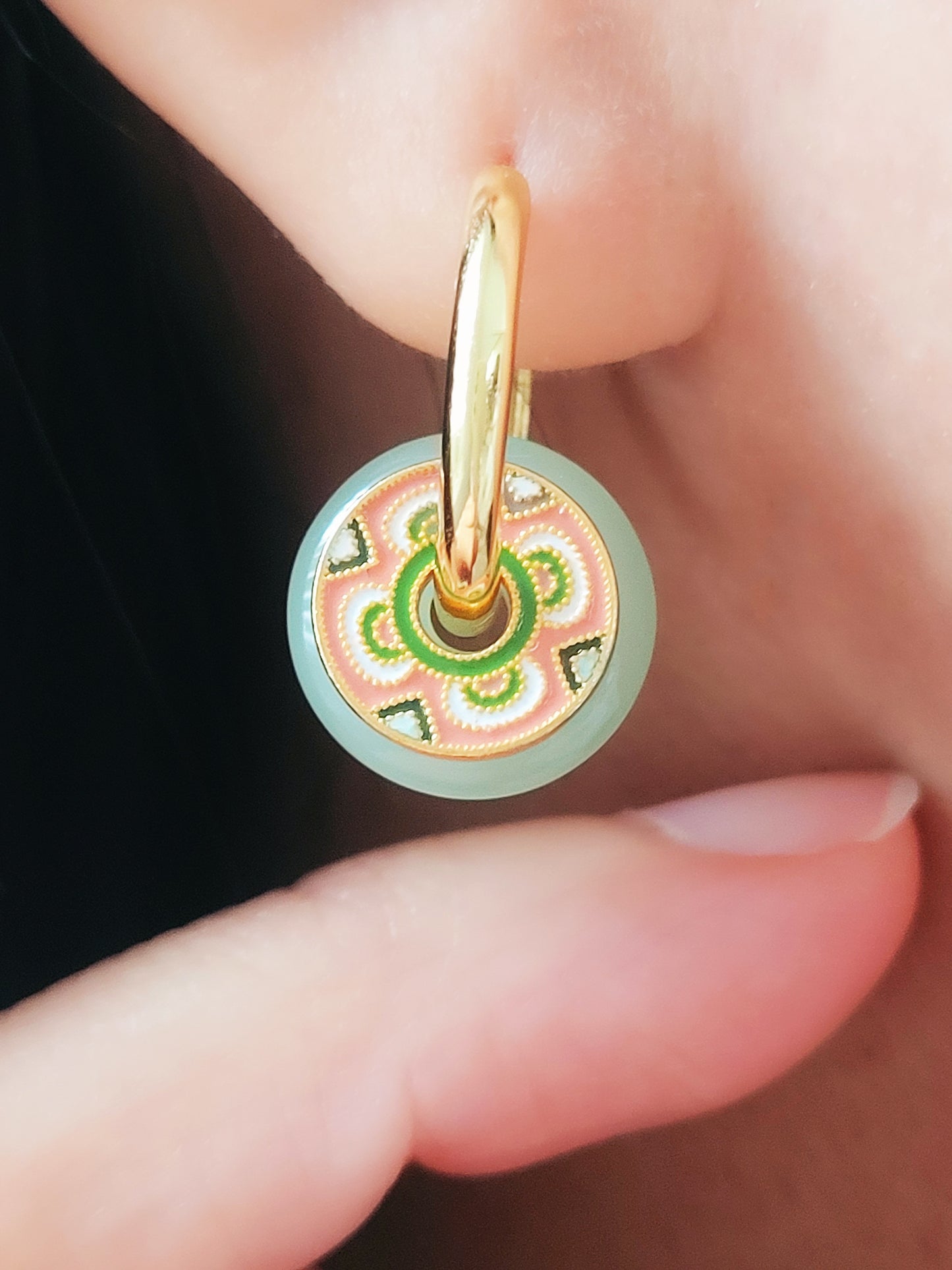 A woman showcases vibrant green jade and pink flower  enamel earrings, featuring tile pattern and jade hoop design.