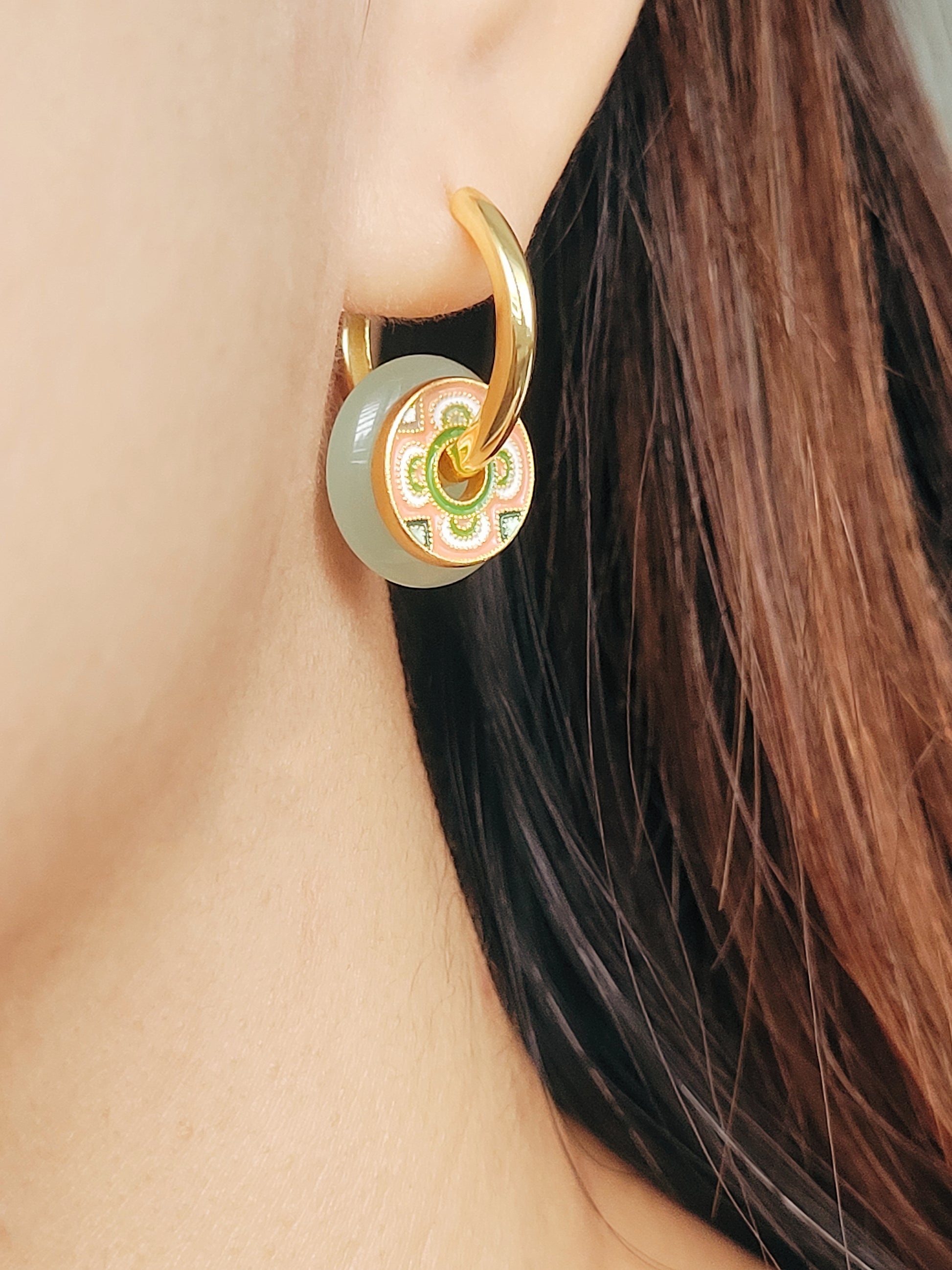 A woman displays stylish green jade with a pink flower enamel disc earrings with a unique tile pattern and elegant hoop drop.