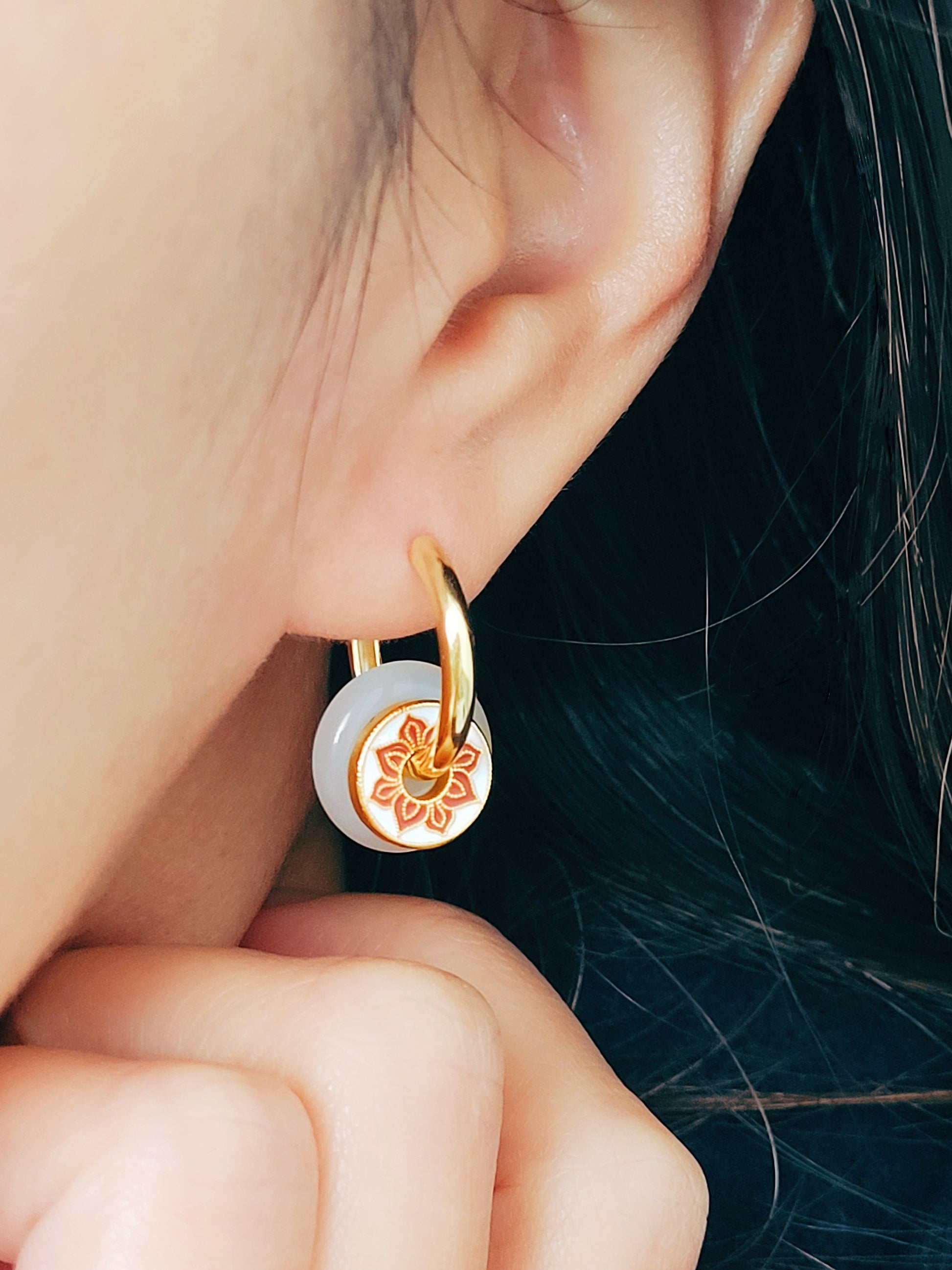 A woman showcasing her stunning and unusual earrings crafted in yellow gold vermeil with jade drop and enamel disc.