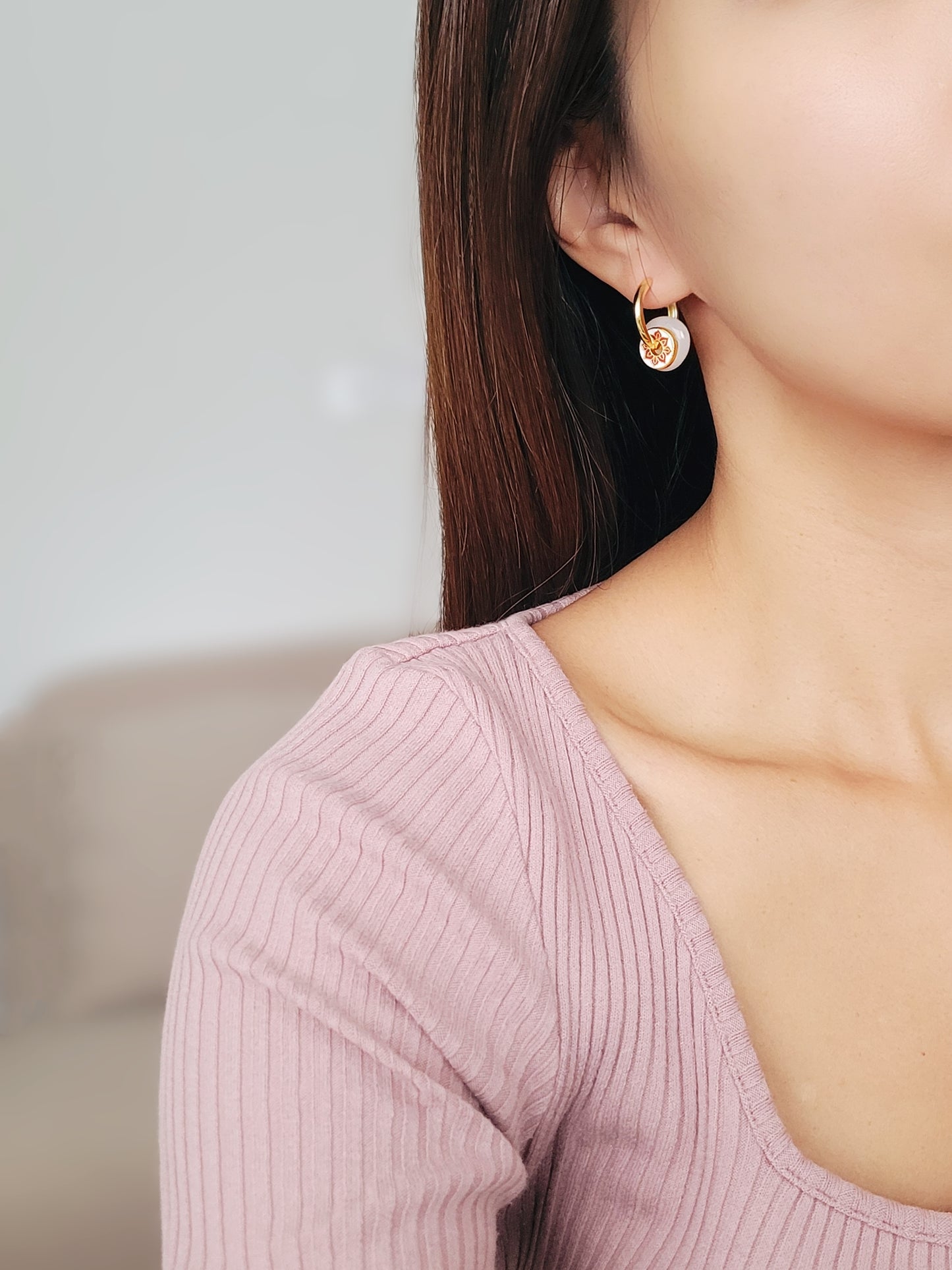 A woman showcasing her stunning and unusual earrings crafted in yellow gold vermeil with jade drop and enamel disc.