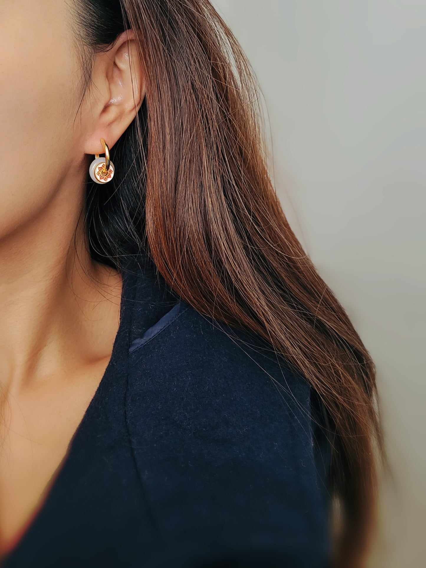 A woman showcasing her stunning and unusual earrings crafted in yellow gold vermeil with jade drop and enamel disc.