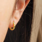 A close-up of a woman's ear displaying a small, dainty 18K gold-plated huggie hoop earring intricately inlaid with tiny turquoise starburst stones.