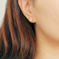 A woman with long hair adorned with a gold tile pattern earring ,exuding elegance and charm.