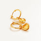 Gold heart dangle earrings with yellow crystal quartz gemstone on a light beige background