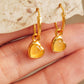 Gold heart crystal earrings held by a hand against a stone background