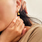 Close-up of a woman wearing gold heart drop earrings with a neutral background