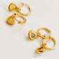 Gold heart earrings with green or yellow stones on a light background